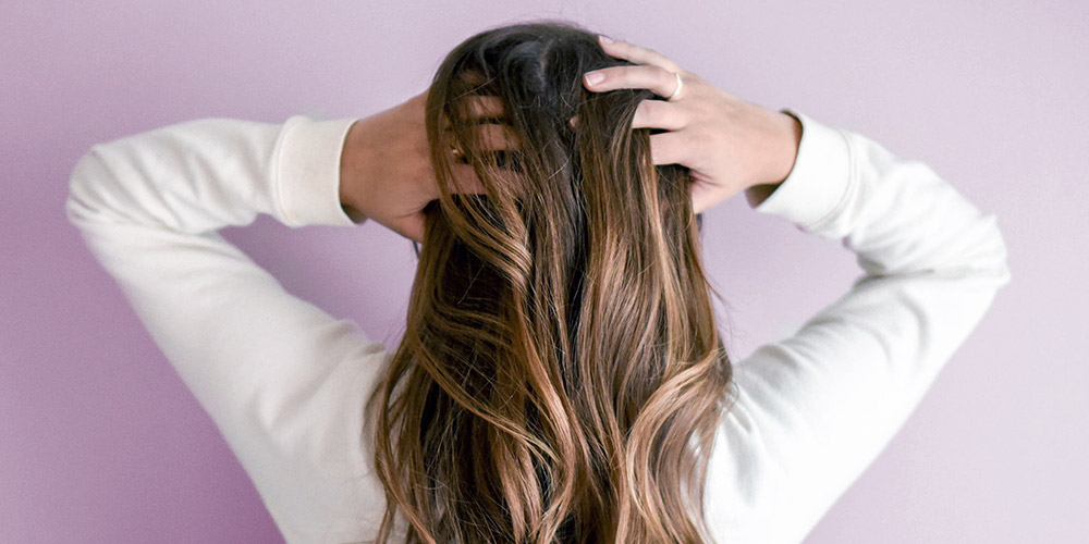 Photo of woman from the back, running her hands through long, brown, wavy hair